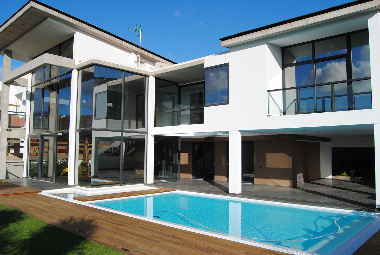 Casa moderna blanca independiente con piscina y zona de relax y grandes ventanas de perfil oscuro.
