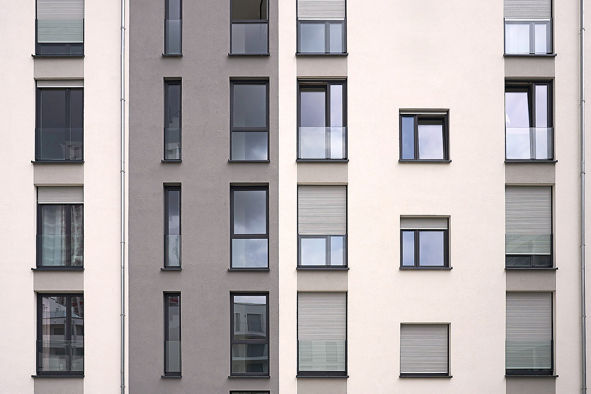 Fachada de edificio marrón arena con dos tonos y ventanas Kömmerling gris oscuro y sistema de persianas VarNova de Kömmerling