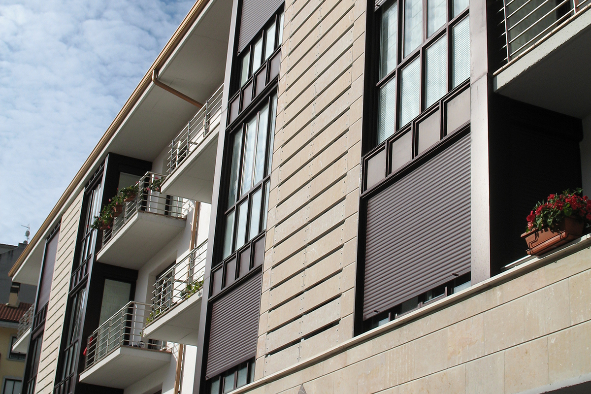 Fachada de edificio marrón de piedra y ventanas marrones oscuras con persianas RolaPlus de Kömmerling