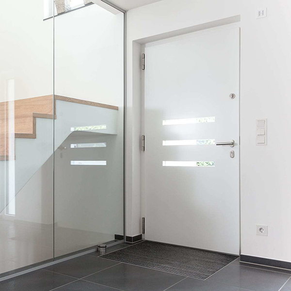 Recibidor principal de una casa de color blanco con la puerta principal en blanco y unas escaleras de madera separadas por un cristal